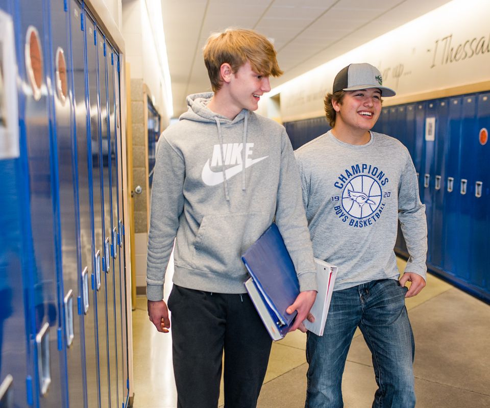two male students walking down a hallway with lockers